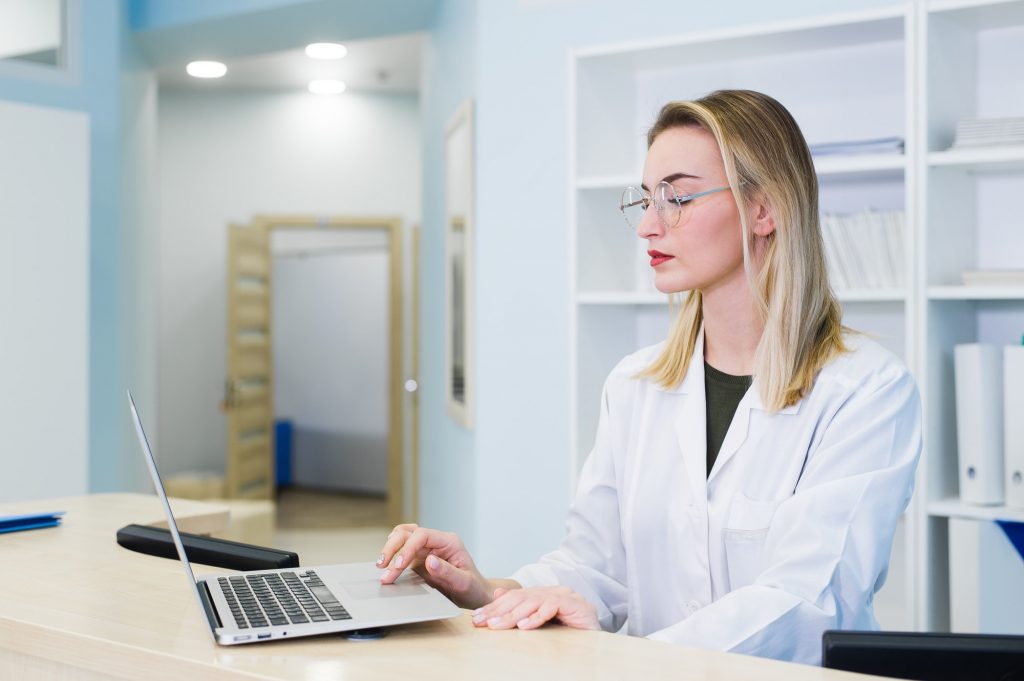 smiling nurse with laptop scheduling appointment for male patient at reception